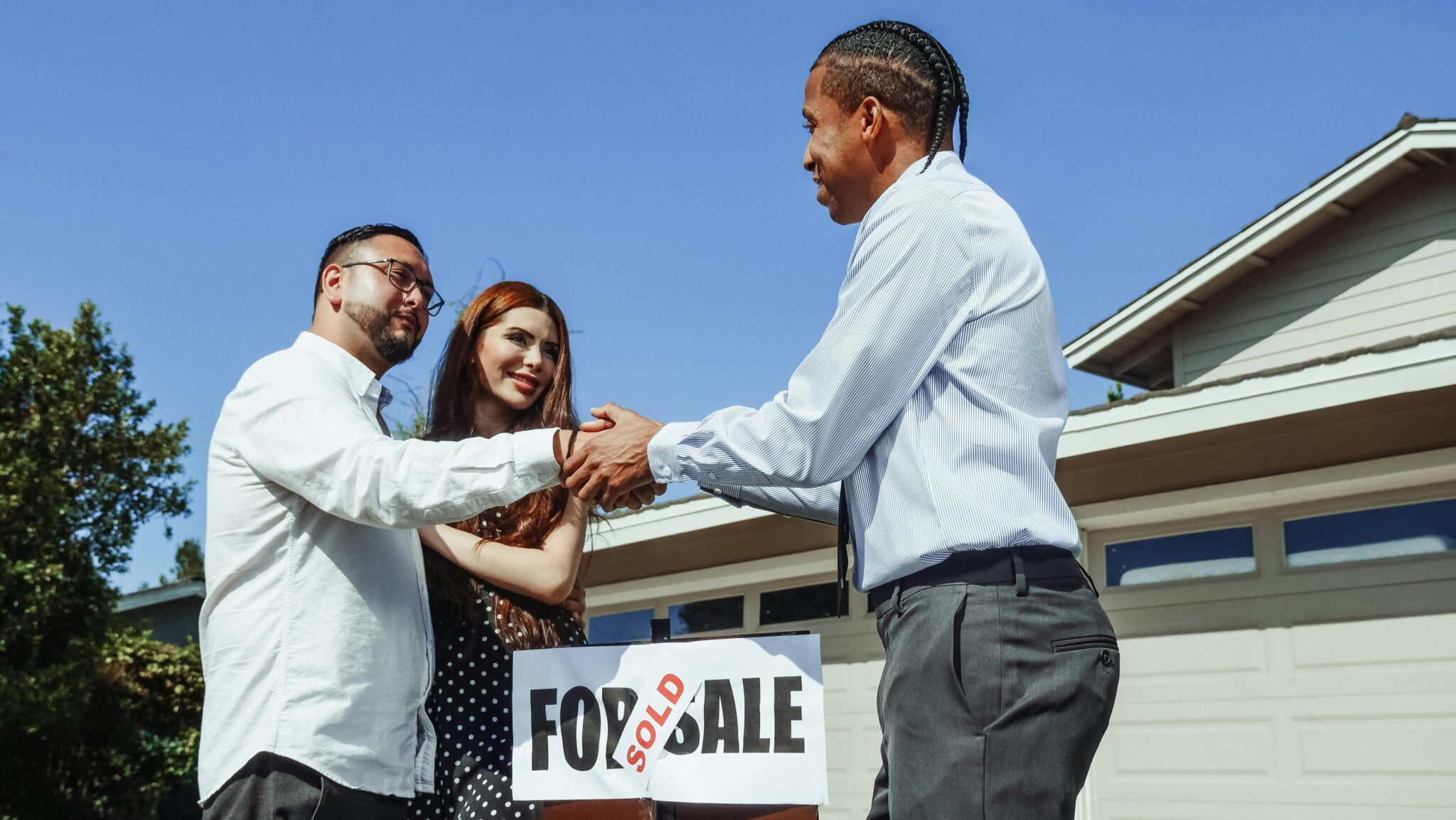 A couple shakes hands with their realtor in front of their newly purchased home.